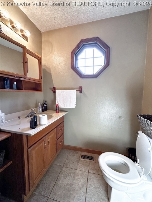 bathroom with tile patterned flooring, a textured ceiling, vanity, and toilet