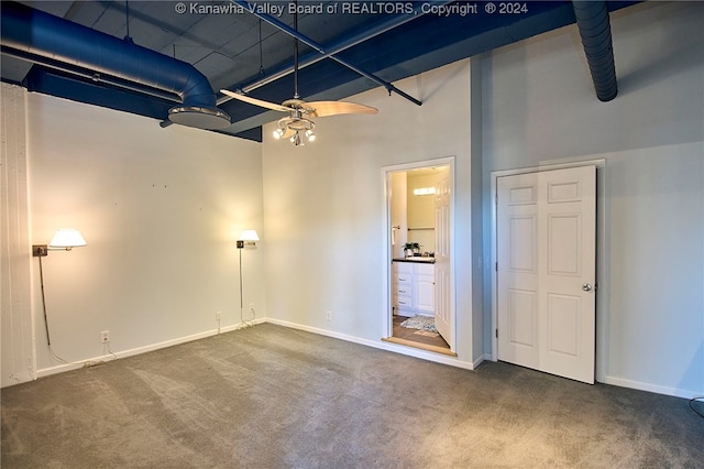 unfurnished bedroom with a high ceiling, dark colored carpet, and ceiling fan