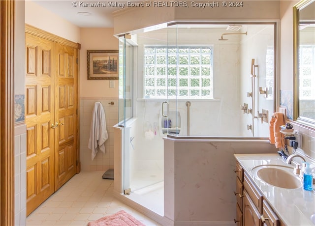 bathroom with tile patterned flooring, a shower with door, vanity, and tile walls