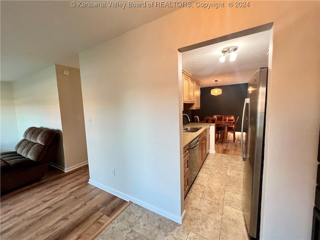 kitchen with sink, decorative light fixtures, light wood-type flooring, and stainless steel appliances