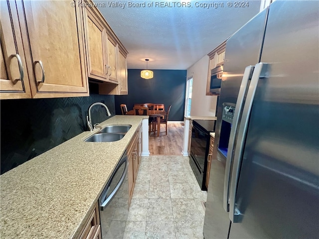 kitchen with light stone countertops, sink, stainless steel appliances, decorative light fixtures, and light hardwood / wood-style flooring