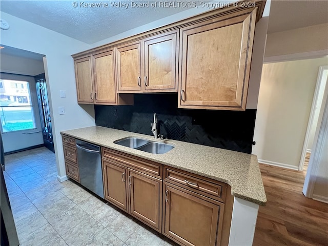 kitchen with dishwasher, sink, light stone counters, light hardwood / wood-style floors, and tasteful backsplash