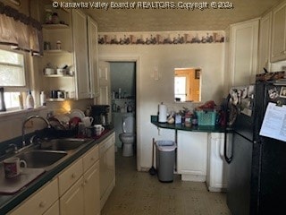 kitchen with black fridge, a wealth of natural light, sink, and white cabinets