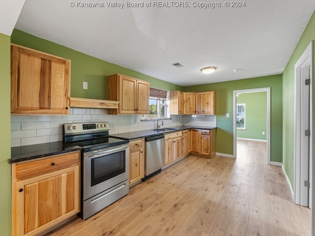 kitchen featuring tasteful backsplash, appliances with stainless steel finishes, light wood-type flooring, dark stone countertops, and sink