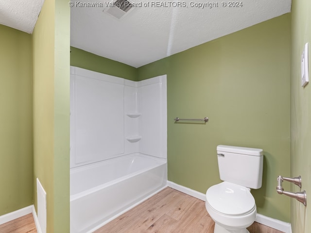 bathroom featuring toilet, hardwood / wood-style flooring, a textured ceiling, and tub / shower combination