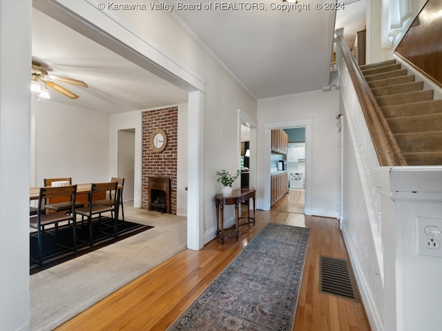 foyer entrance featuring hardwood / wood-style floors, a brick fireplace, and ceiling fan