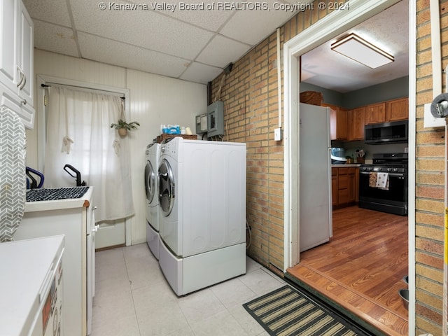 laundry area featuring separate washer and dryer, light wood-type flooring, wood walls, sink, and brick wall