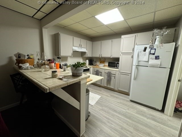 kitchen featuring a drop ceiling, tile countertops, pendant lighting, white fridge, and light hardwood / wood-style flooring