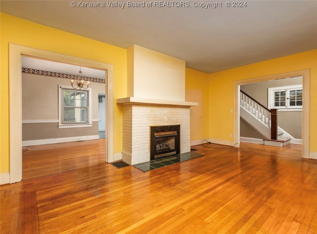 unfurnished living room featuring hardwood / wood-style flooring, an inviting chandelier, and a brick fireplace