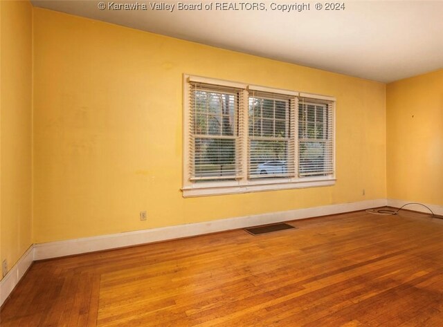 empty room featuring hardwood / wood-style floors, visible vents, and baseboards