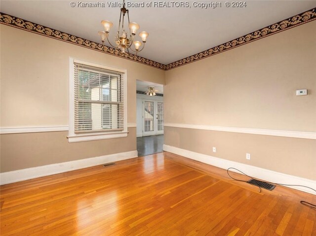 empty room featuring baseboards, wood finished floors, visible vents, and an inviting chandelier