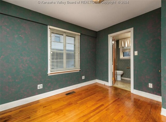 unfurnished bedroom with baseboards, ensuite bathroom, visible vents, and wood-type flooring