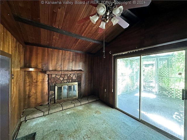 unfurnished living room with ceiling fan, wooden ceiling, vaulted ceiling, a stone fireplace, and wooden walls