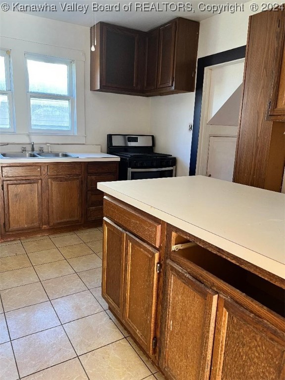 kitchen featuring stainless steel gas range oven, light tile patterned floors, and sink