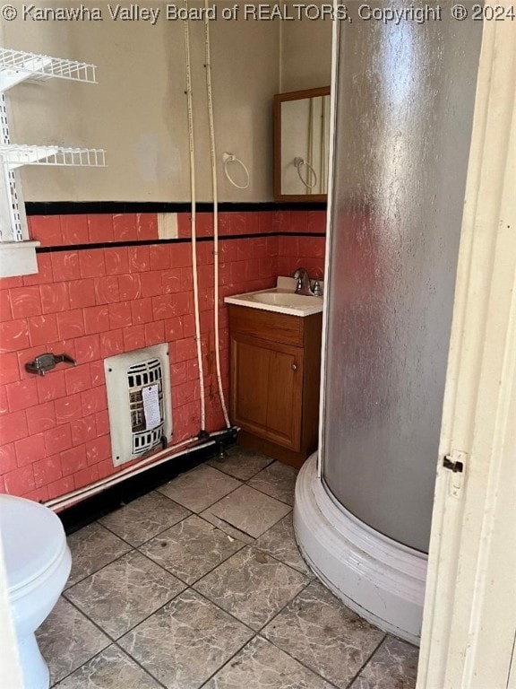 bathroom with heating unit, a shower with door, vanity, and tile walls