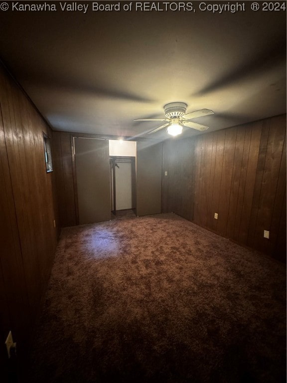 basement featuring ceiling fan, carpet, and wooden walls