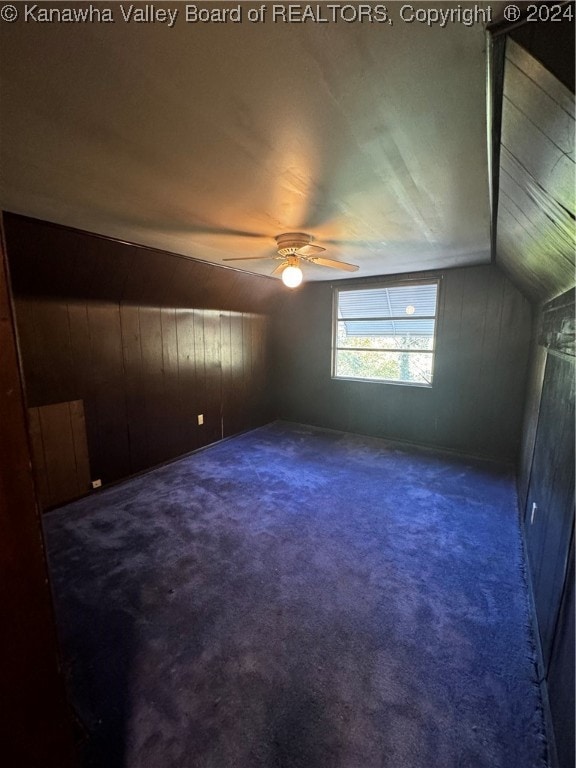 bonus room featuring dark carpet, vaulted ceiling, ceiling fan, and wood walls