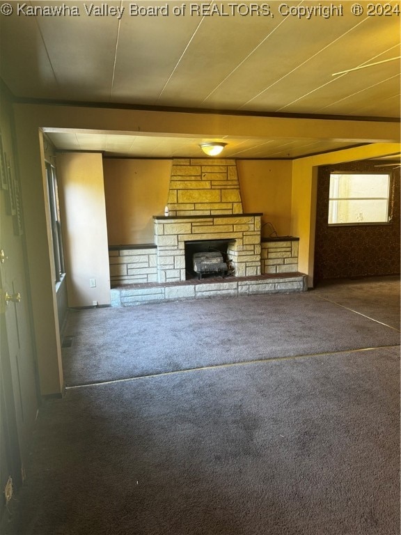 unfurnished living room with a stone fireplace and dark colored carpet