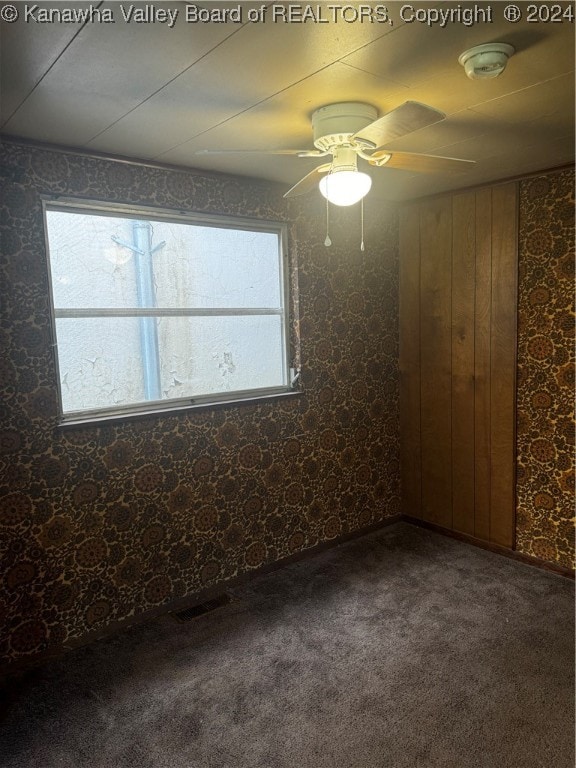 empty room with wooden walls, carpet, and ceiling fan