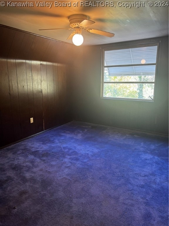 carpeted empty room featuring ceiling fan and wooden walls