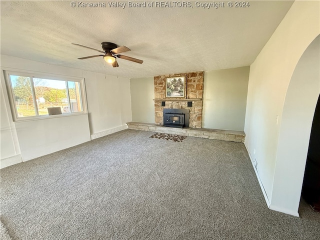 unfurnished living room with a wood stove, a textured ceiling, carpet flooring, and ceiling fan