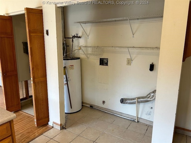 clothes washing area featuring electric dryer hookup, light tile patterned flooring, and water heater