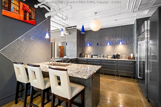 kitchen with gray cabinetry, light stone countertops, a kitchen bar, built in fridge, and decorative light fixtures