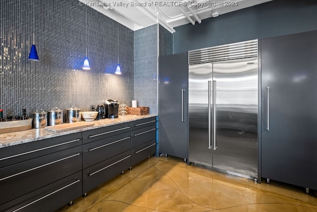 kitchen with backsplash, stainless steel built in refrigerator, tile walls, decorative light fixtures, and light stone counters