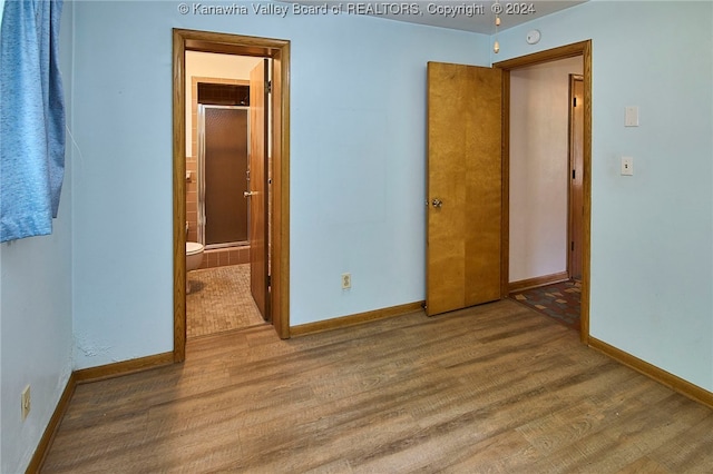 unfurnished bedroom with ensuite bathroom and hardwood / wood-style flooring