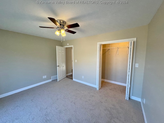 unfurnished bedroom with a textured ceiling, light colored carpet, a closet, and ceiling fan