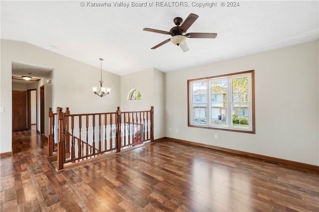 empty room featuring lofted ceiling, ceiling fan with notable chandelier, and dark hardwood / wood-style flooring