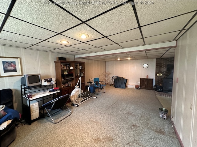 home office with a drop ceiling, a wood stove, and carpet