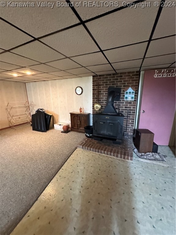 basement featuring a paneled ceiling, a wood stove, and carpet floors