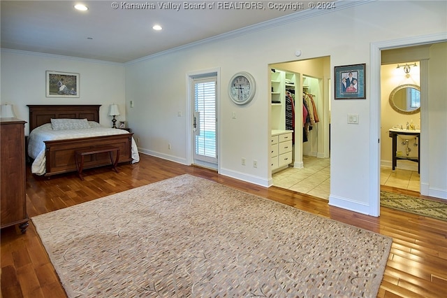 bedroom featuring a closet, ensuite bath, a spacious closet, crown molding, and light hardwood / wood-style floors