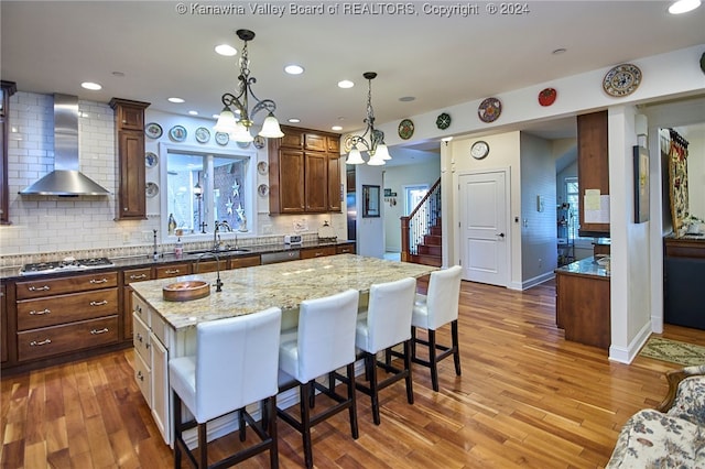 kitchen with wall chimney exhaust hood, wood-type flooring, and a kitchen island