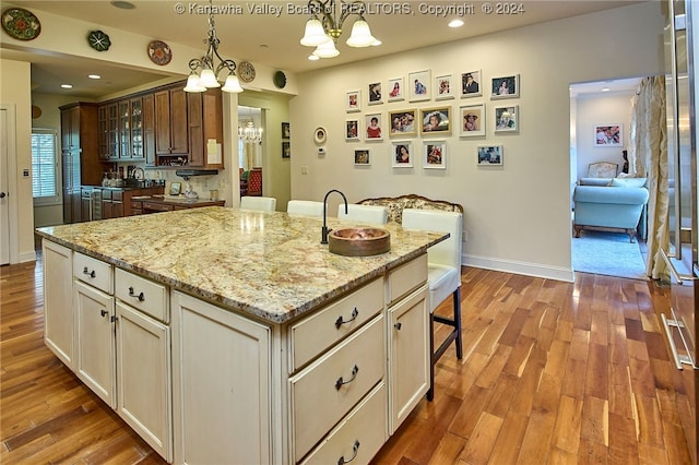 kitchen with light hardwood / wood-style flooring, pendant lighting, a breakfast bar, a chandelier, and a kitchen island with sink