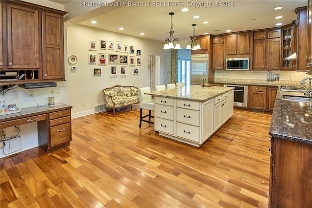 kitchen featuring light stone counters, an island with sink, stainless steel appliances, light hardwood / wood-style floors, and decorative light fixtures