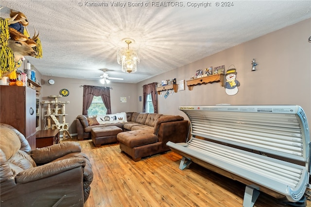 living room featuring hardwood / wood-style flooring, ceiling fan with notable chandelier, and a textured ceiling