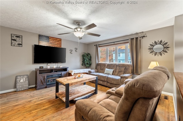 living room featuring a fireplace, ceiling fan, a textured ceiling, and light wood-type flooring