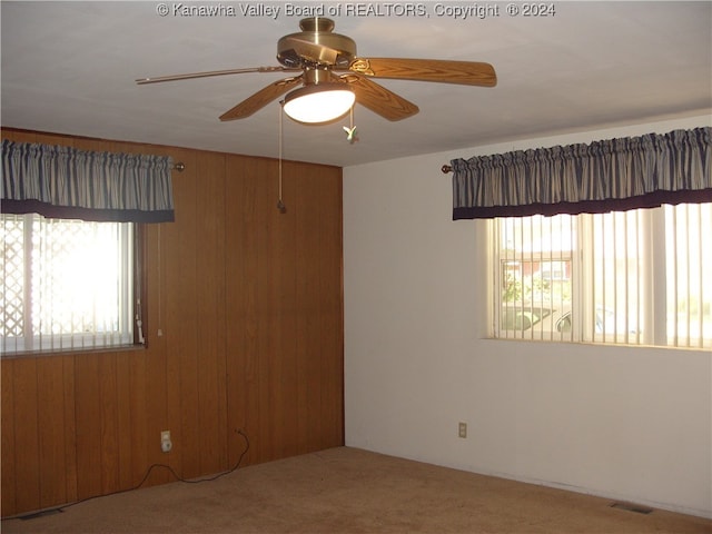 empty room featuring wood walls, ceiling fan, and carpet floors