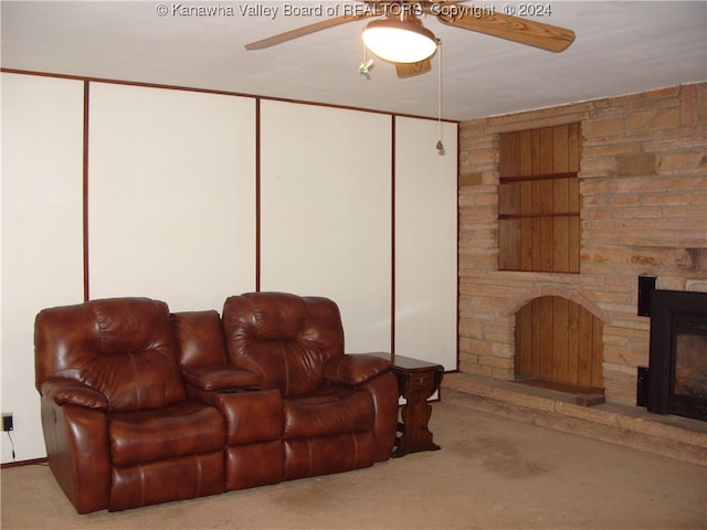 carpeted living room with a stone fireplace, built in features, and ceiling fan