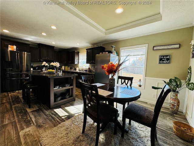 dining room featuring dark wood-type flooring, a textured ceiling, ornamental molding, and a tray ceiling