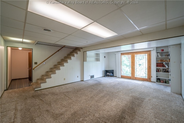 basement with a paneled ceiling, a wood stove, and carpet