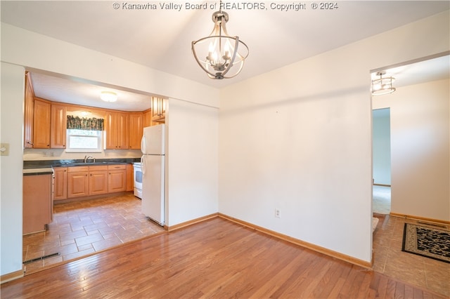 kitchen with hanging light fixtures, an inviting chandelier, sink, white appliances, and light hardwood / wood-style flooring