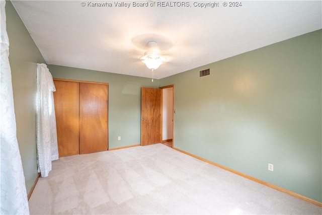 unfurnished bedroom featuring ceiling fan, light carpet, and a closet