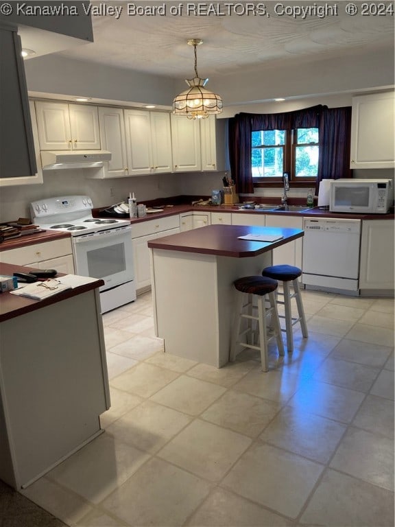 kitchen featuring a kitchen bar, a center island, white cabinets, hanging light fixtures, and white appliances