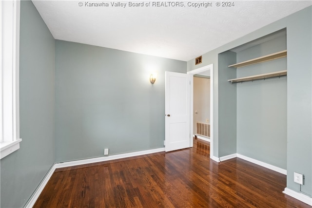 unfurnished bedroom with dark wood-type flooring, a textured ceiling, and a closet