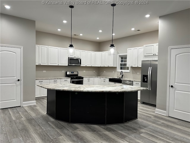 kitchen with stainless steel appliances, a center island, light stone counters, pendant lighting, and light hardwood / wood-style flooring