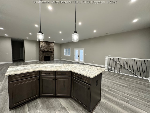 kitchen featuring a stone fireplace, a kitchen island, decorative light fixtures, dark brown cabinetry, and light hardwood / wood-style floors