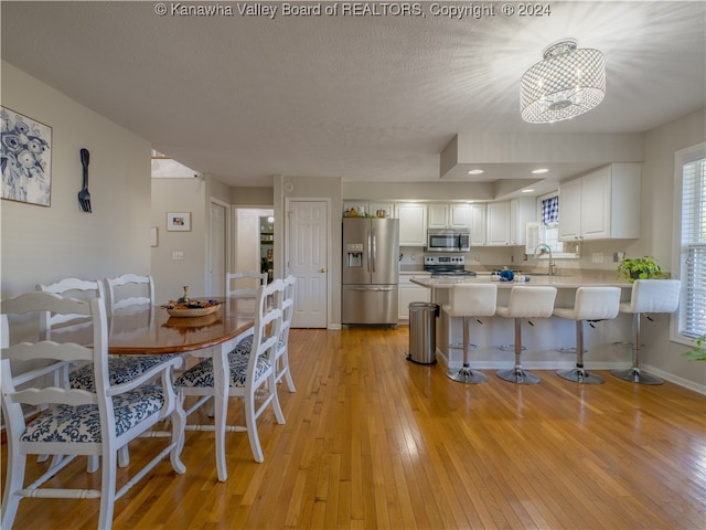 dining room featuring a textured ceiling, light hardwood / wood-style floors, sink, and an inviting chandelier